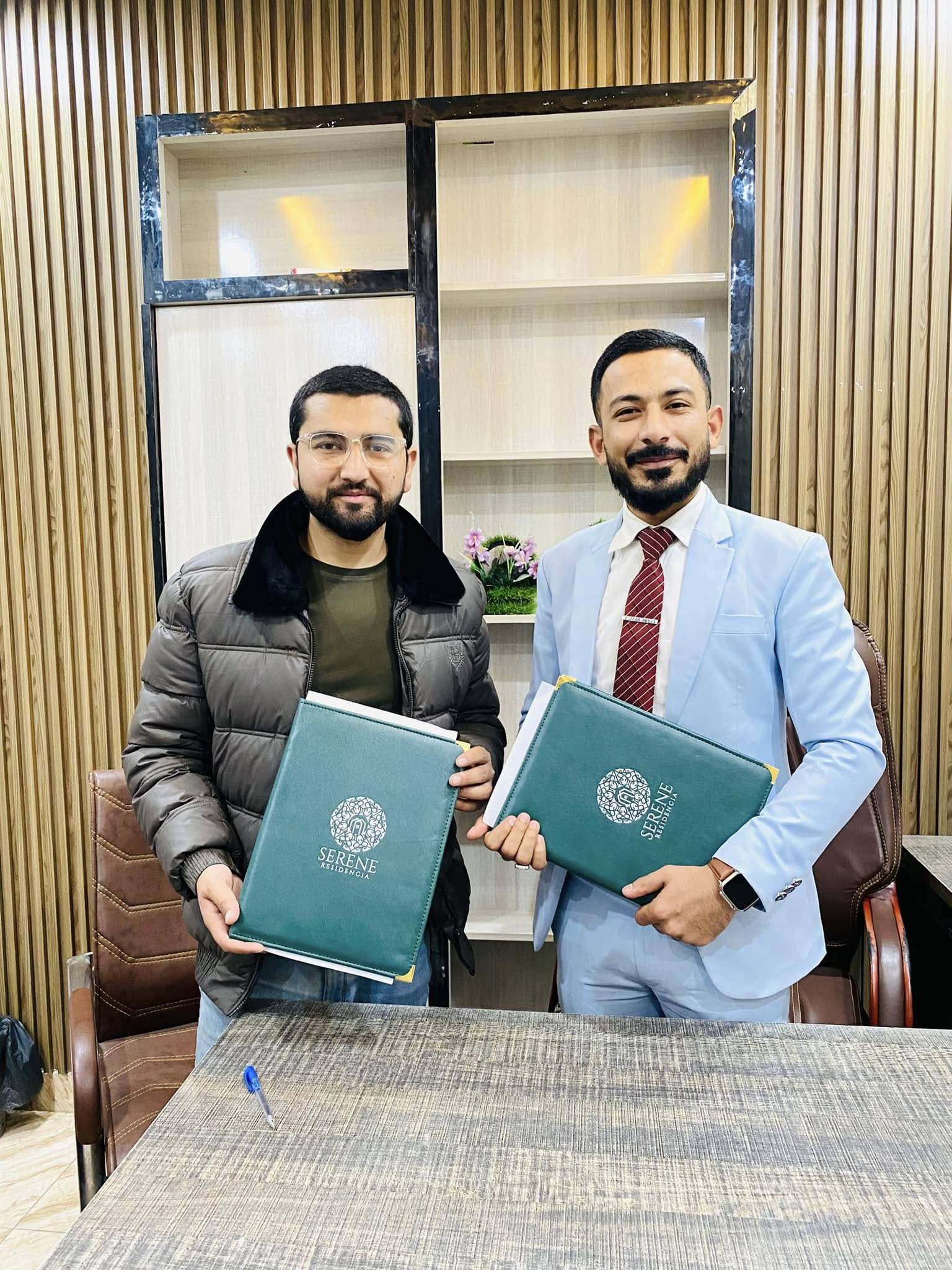 Zafar Abbas Karbalai presenting a Serene Residencia folder with a partner